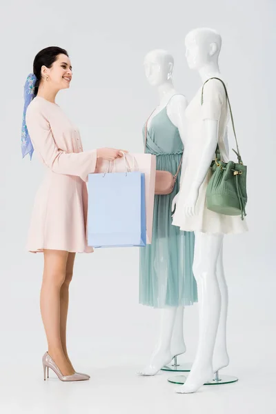 Jeune femme souriante avec des sacs à provisions près de mannequins isolés sur gris — Photo de stock