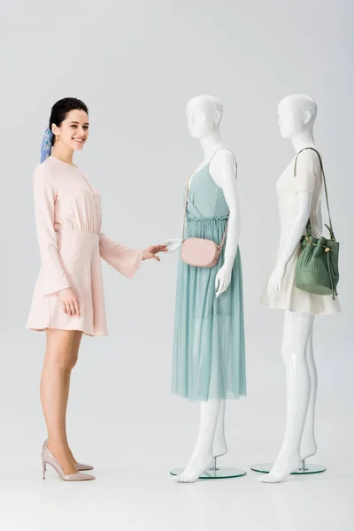 Beautiful smiling girl looking at camera near mannequins in dresses on grey — Stock Photo