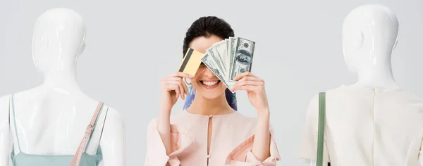 Panoramic shot of girl near mannequins covering face with money and credit card isolated on grey — Stock Photo