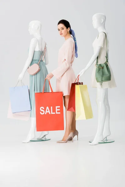 Красива молода жінка зі словом продаж на сумці біля манекенів на сірому — стокове фото