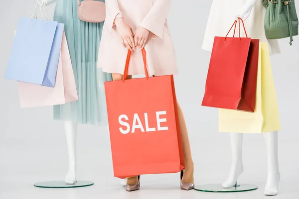 Partial view of young woman with sale lettering on shopping bag near mannequins on grey — Stock Photo