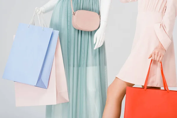Vista recortada de mujer joven y maniquí con bolsas de compras aisladas en gris - foto de stock