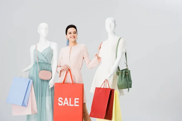 Schöne junge Frau mit Verkauf Schriftzug auf Einkaufstasche in der Nähe Schaufensterpuppen isoliert auf grau — Stockfoto