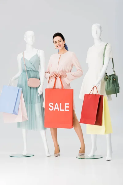 Schöne junge Frau mit Verkauf Schriftzug auf Einkaufstasche in der Nähe von Schaufensterpuppen auf grau — Stockfoto