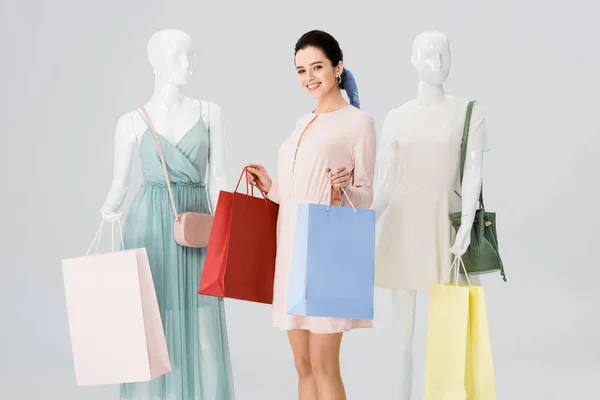 Belle fille souriante avec des sacs à provisions près de mannequins isolés sur gris — Photo de stock