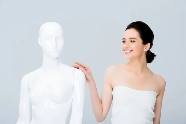Приваблива усміхнена молода жінка в білому позуванні з манекеном ізольована на сірому — стокове фото