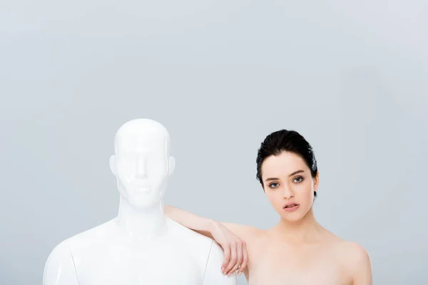 Beautiful girl leaning on mannequin and looking at camera isolated on grey — Stock Photo