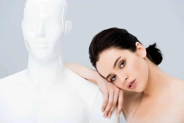 Beautiful young woman leaning on mannequin and looking at camera isolated on grey — Stock Photo