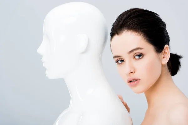 Attractive young woman posing with plastic mannequin and looking at camera isolated on grey — Stock Photo