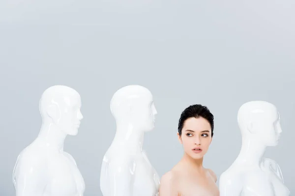 Hermosa chica desnuda cerca de maniquíes blancos aislados en gris — Stock Photo