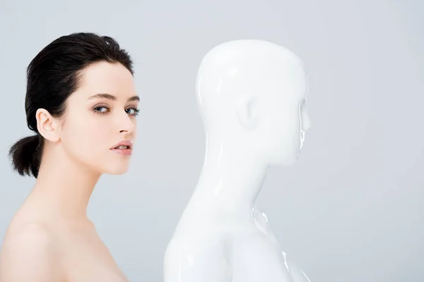 Beautiful young woman looking at camera and posing with mannequin isolated on grey — Stock Photo