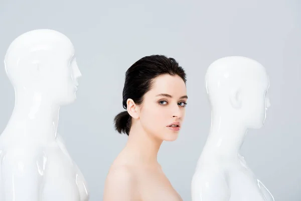 Красива дівчина біля білих манекенів дивиться на камеру ізольовано на сірому — стокове фото