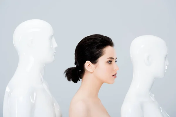 Nude young woman posing in row of mannequins isolated on grey — Stock Photo