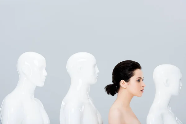 Оголена молода жінка позує в ряд манекенів ізольовано на сірому — стокове фото