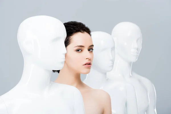 Beautiful nude girl posing in row of mannequins isolated on grey — Stock Photo