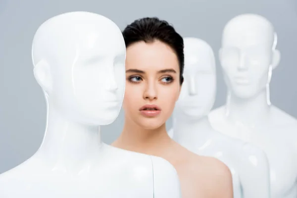 Beautiful girl posing in row of mannequins isolated on grey — Stock Photo