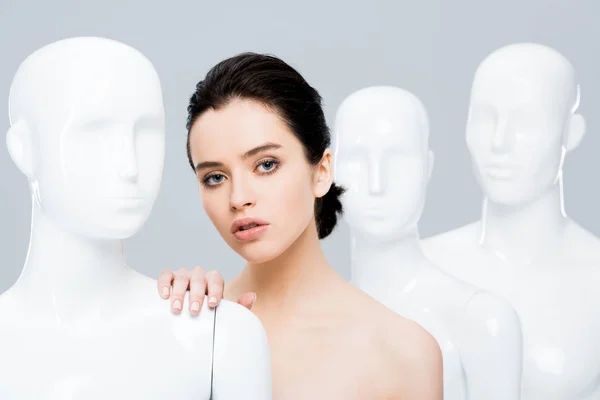 Beautiful young woman posing with mannequins isolated on grey — Stock Photo