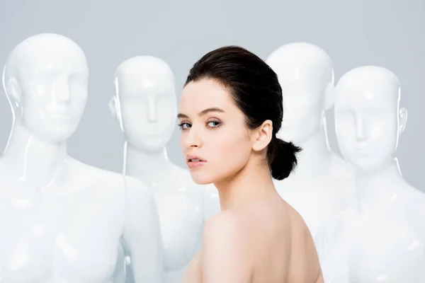 Красивая голая девушка смотрит в камеру, позируя рядом с манекенами, изолированными на сером — стоковое фото