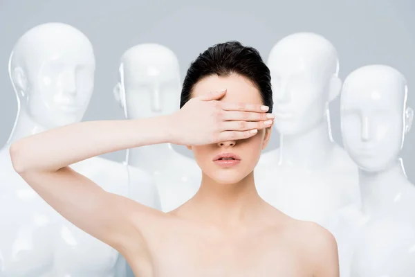 Hermosa chica cubriendo la cara con la mano cerca de maniquíes aislados en gris - foto de stock