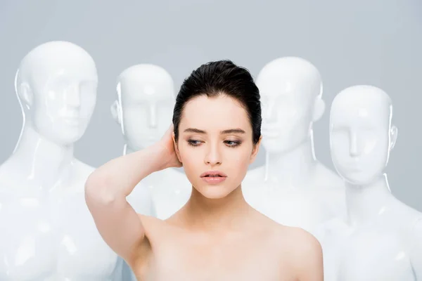 Beautiful young woman posing near mannequins isolated on grey — Stock Photo