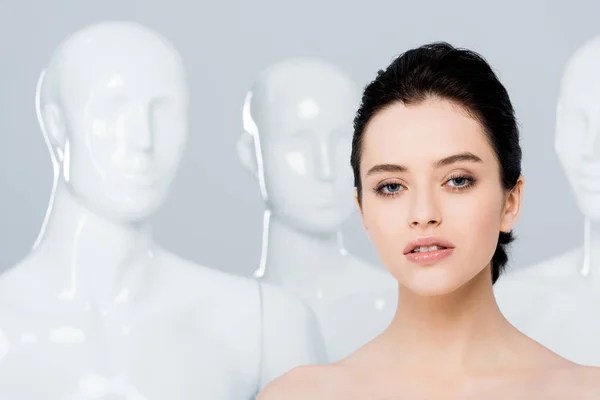 Beautiful naked young woman looking at camera near mannequins isolated on grey — Stock Photo