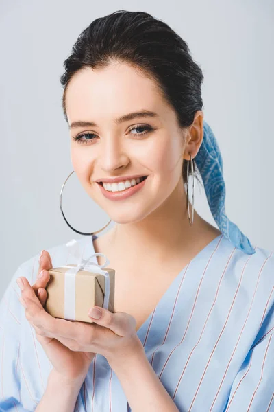 Hermosa chica elegante con caja de regalo sonriendo y mirando a la cámara aislada en gris - foto de stock