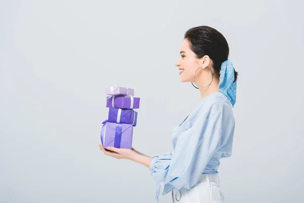 Side view of beautiful stylish girl holding gift boxes isolated on grey — Stock Photo