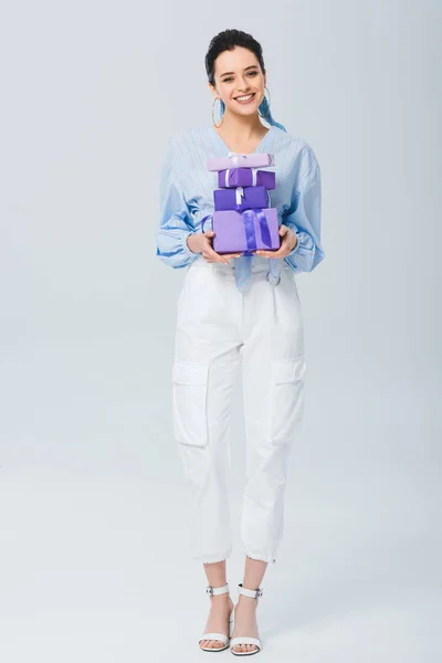 Hermosa chica elegante sosteniendo cajas de regalo y sonriendo en gris - foto de stock