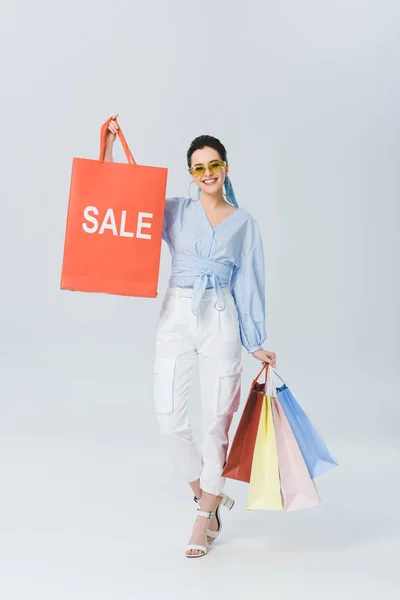 Smiling stylish girl holding shopping bag with sale word on grey — Stock Photo