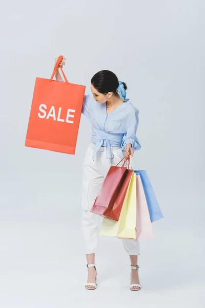 Beautiful stylish girl holding shopping bag with sale word on grey — Stock Photo
