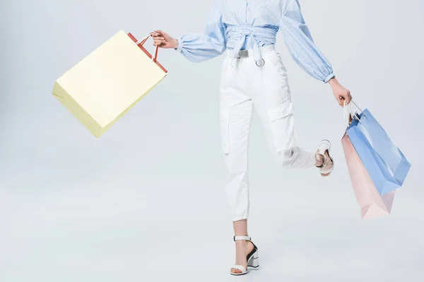 Vista recortada de chica elegante caminando con bolsas de compras en gris - foto de stock