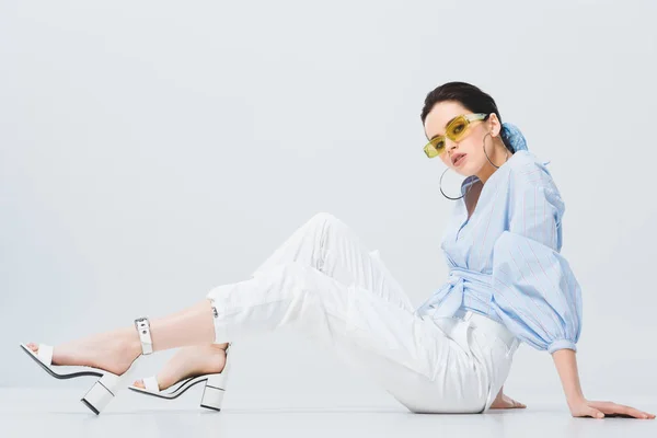 Hermosa chica con estilo en gafas de sol sentado y posando en gris — Stock Photo
