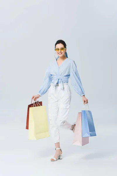 Belle fille souriante avec des sacs à provisions marchant sur gris — Photo de stock