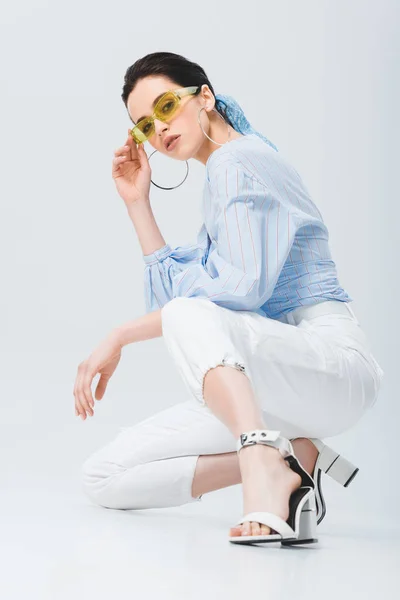 Schöne stylische Mädchen mit Sonnenbrille sitzt und posiert auf grau — Stockfoto