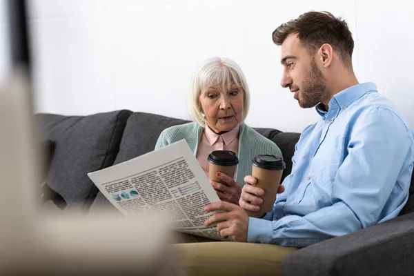 Mann und Seniorin halten zu Hause Kaffee und lesen Zeitung — Stockfoto