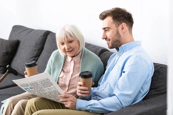 Hombre y madre mayor sosteniendo café y leyendo el periódico en casa - foto de stock