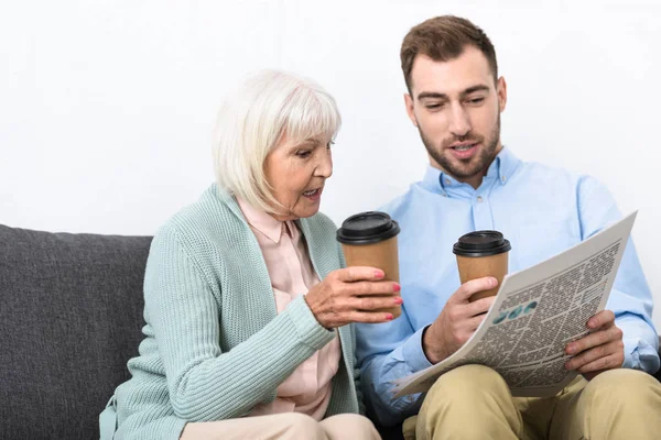 Мужчина и старшая мать держат чашки кофе и читают газеты дома — стоковое фото