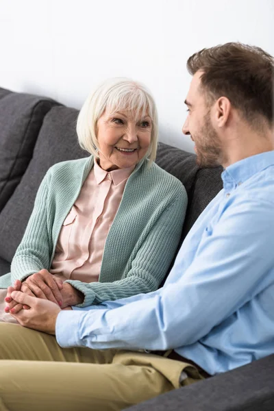 Smiling senior mother and son holding hands and looking at each other — Stock Photo