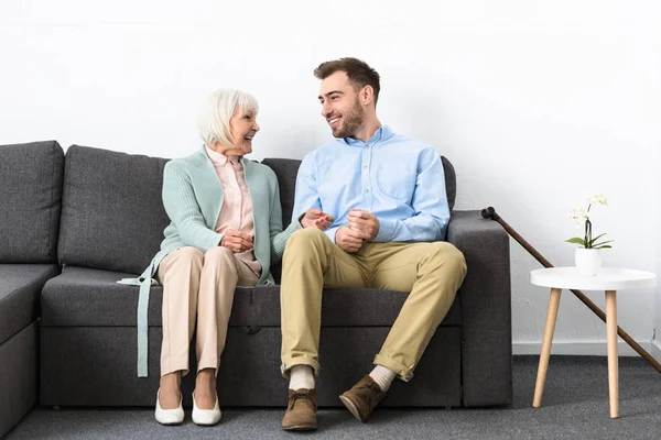 Lächelnde Seniorin und ihr Sohn schauen sich auf dem Sofa an — Stockfoto