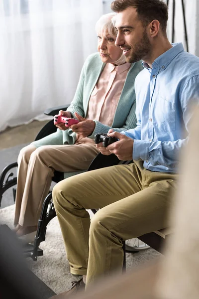 KYIV, UKRAINE - 15 de abril de 2019: mulher idosa com deficiência e filho jogando videogame com joysticks — Fotografia de Stock