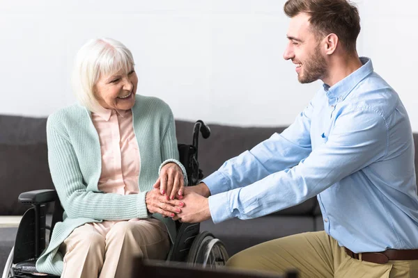 Sonriente hombre barbudo cogido de la mano con madre mayor discapacitada - foto de stock