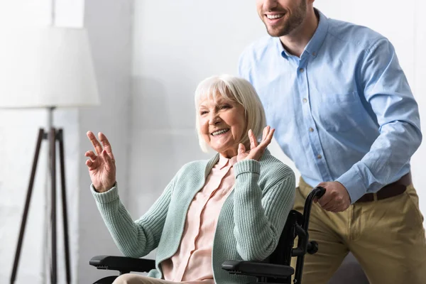 Vista parcial del hombre portador de una madre anciana discapacitada en silla de ruedas - foto de stock
