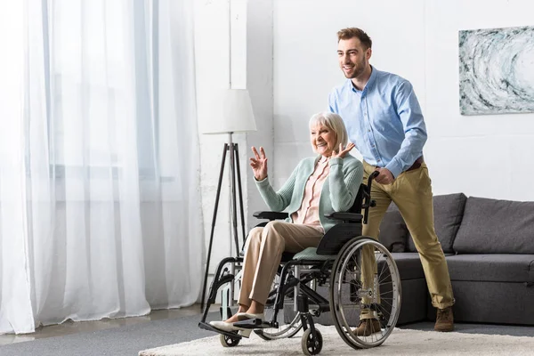 Lächelnder Mann trägt behinderte Seniorin im Rollstuhl — Stockfoto