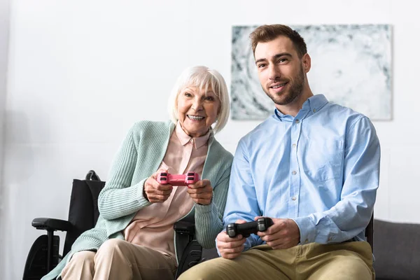 KYIV, UCRANIA - 15 DE ABRIL DE 2019: una alegre anciana discapacitada con un hijo sonriente jugando videojuegos - foto de stock