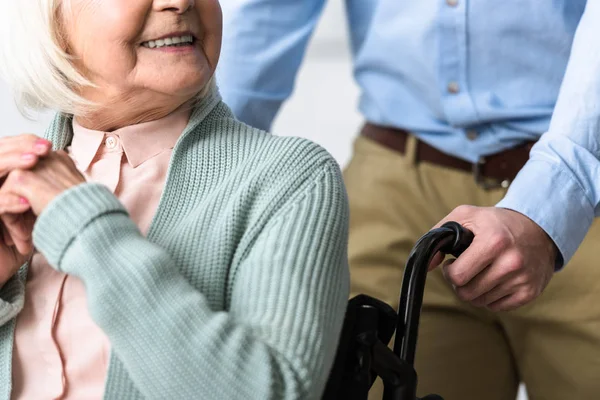 Vista recortada del hombre que lleva a la madre mayor discapacitada en silla de ruedas - foto de stock