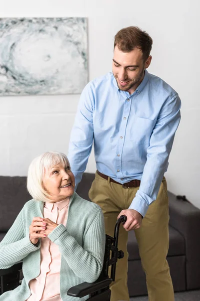 Smiling man carrying disabled senior mother on wheelchair — Stock Photo