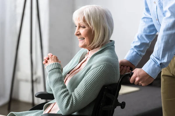 Vue recadrée de l'homme portant une mère aînée handicapée en fauteuil roulant — Photo de stock