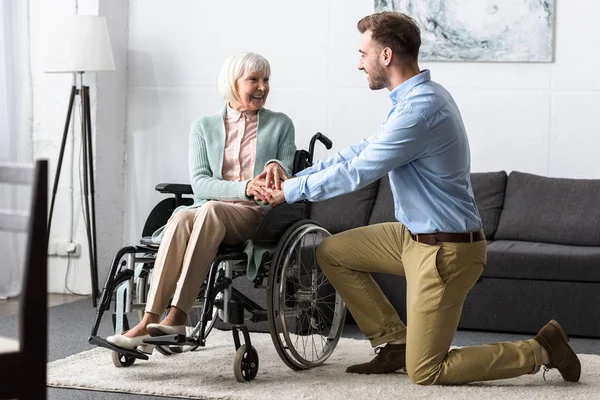 Behinderte Seniorin im Rollstuhl und lächelnder Mann schauen einander an — Stockfoto