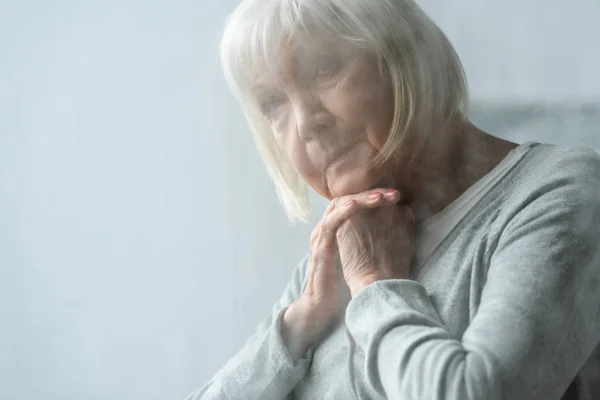 Selective focus of pensive senior woman with grey hair propping face with hands — Stock Photo