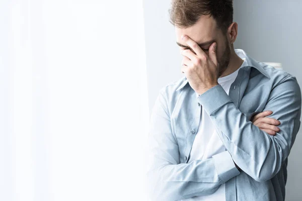 Depressed man in blue shirt covering face with hand on at home — Stock Photo